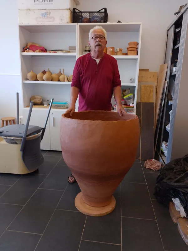 Daniel Caselles de pie junto a una tinaja de barro urdida que le llega a la cintura, en su taller