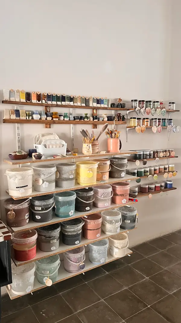Estantería con botes de esmaltes, muestras de color y cubos de barro del taller