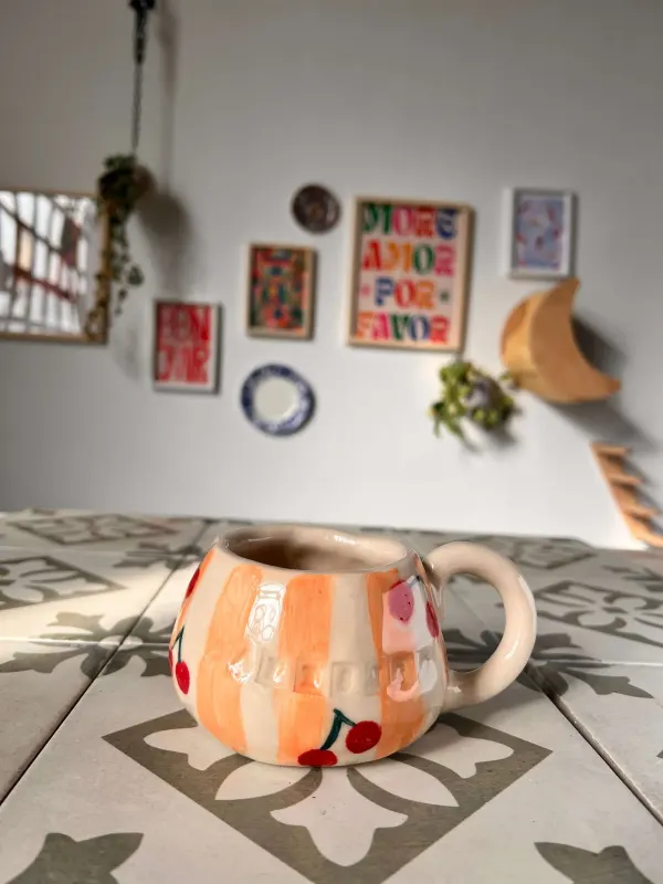 Taza de cerámica pintada a mano con rayas naranjas y cerezas rojas, con el asa redonda